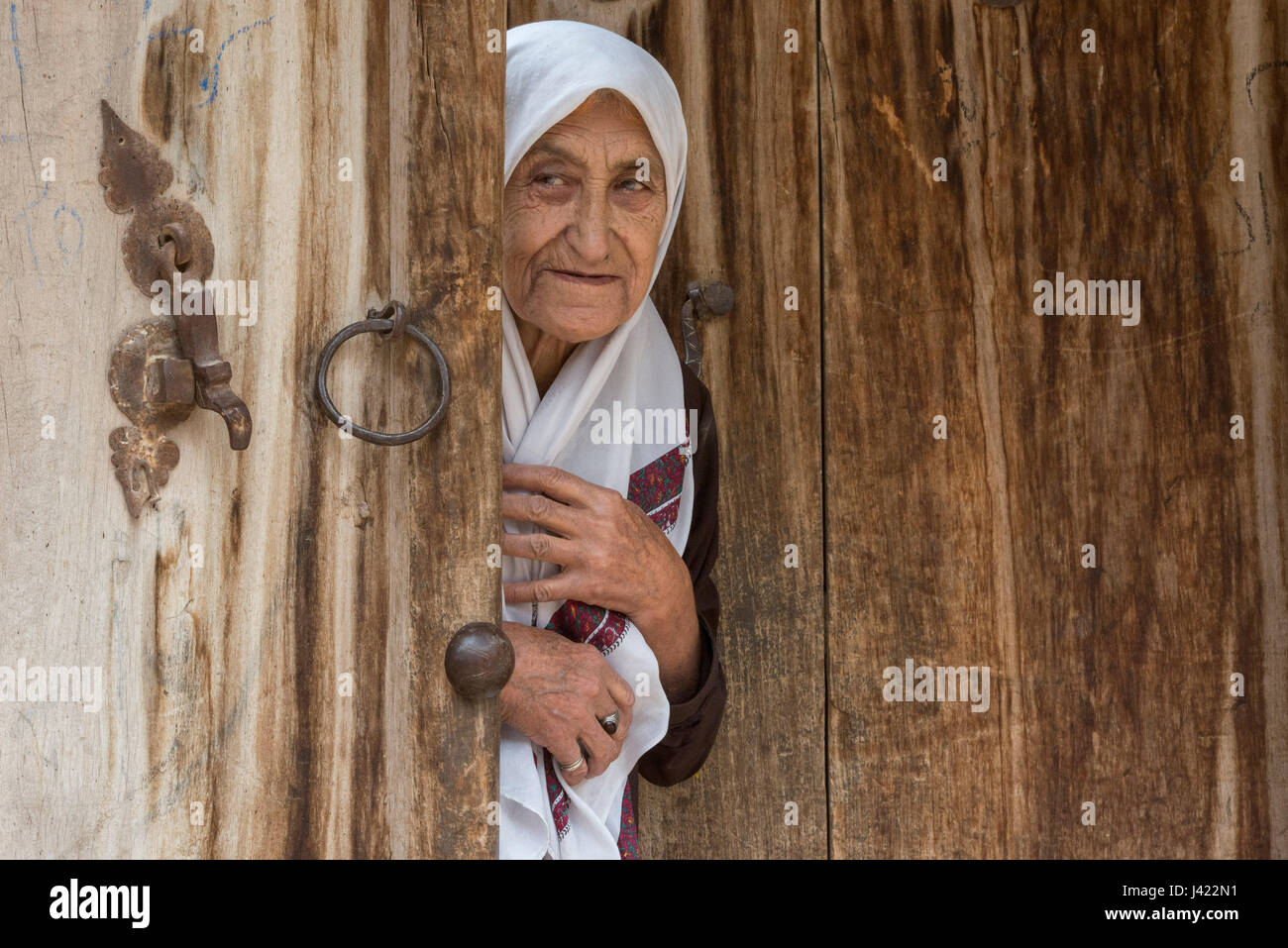 Old Lady Opening Up Wooden Doors Of Her House, Esfidan, A Traditional Rural Village, North Khorasan Province, IRAN Stock Photo