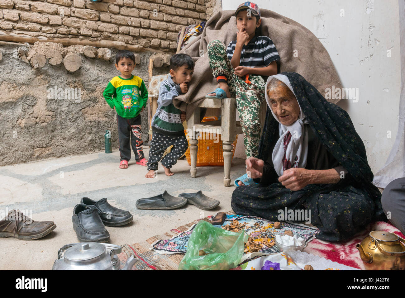 Old Lady And Grandsons Inside Her House Offering Homemade Delicacies To Visitors, Esfidan, A Traditional Rural Village, North Khorasan Province, IRAN  Stock Photo
