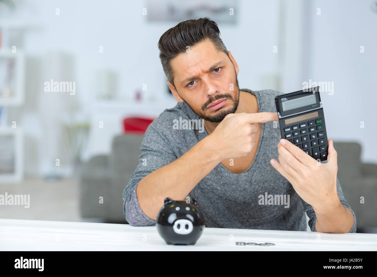 man with piggy bank looking sadly at calculator Stock Photo - Alamy