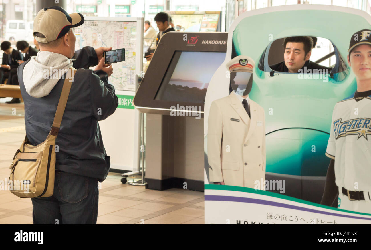 Hakodate, Japan - April 3th, 2017: A japanese man taking a photo of a friend with his mobile inside a JR Hokkaido shinkansen train publicity at the JR Stock Photo