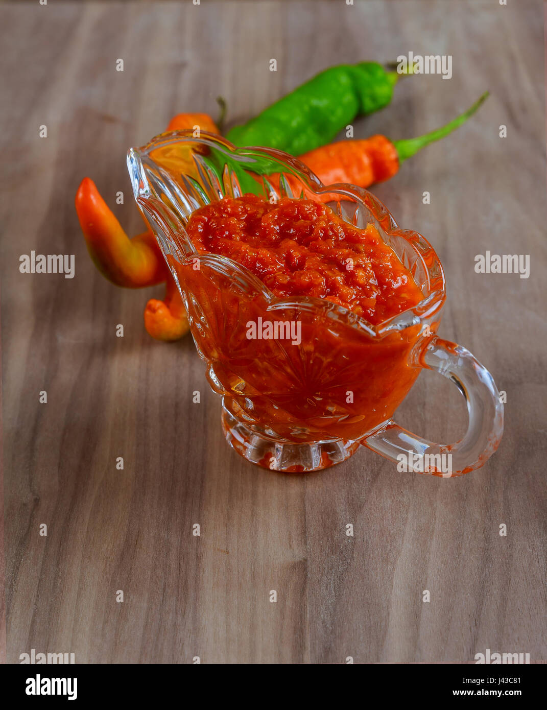 Tabasco adjika in a glass gravy boat, hot pepper, garlic, parsley, fenugreek, oil in the decanter on the background of sack cloth Stock Photo