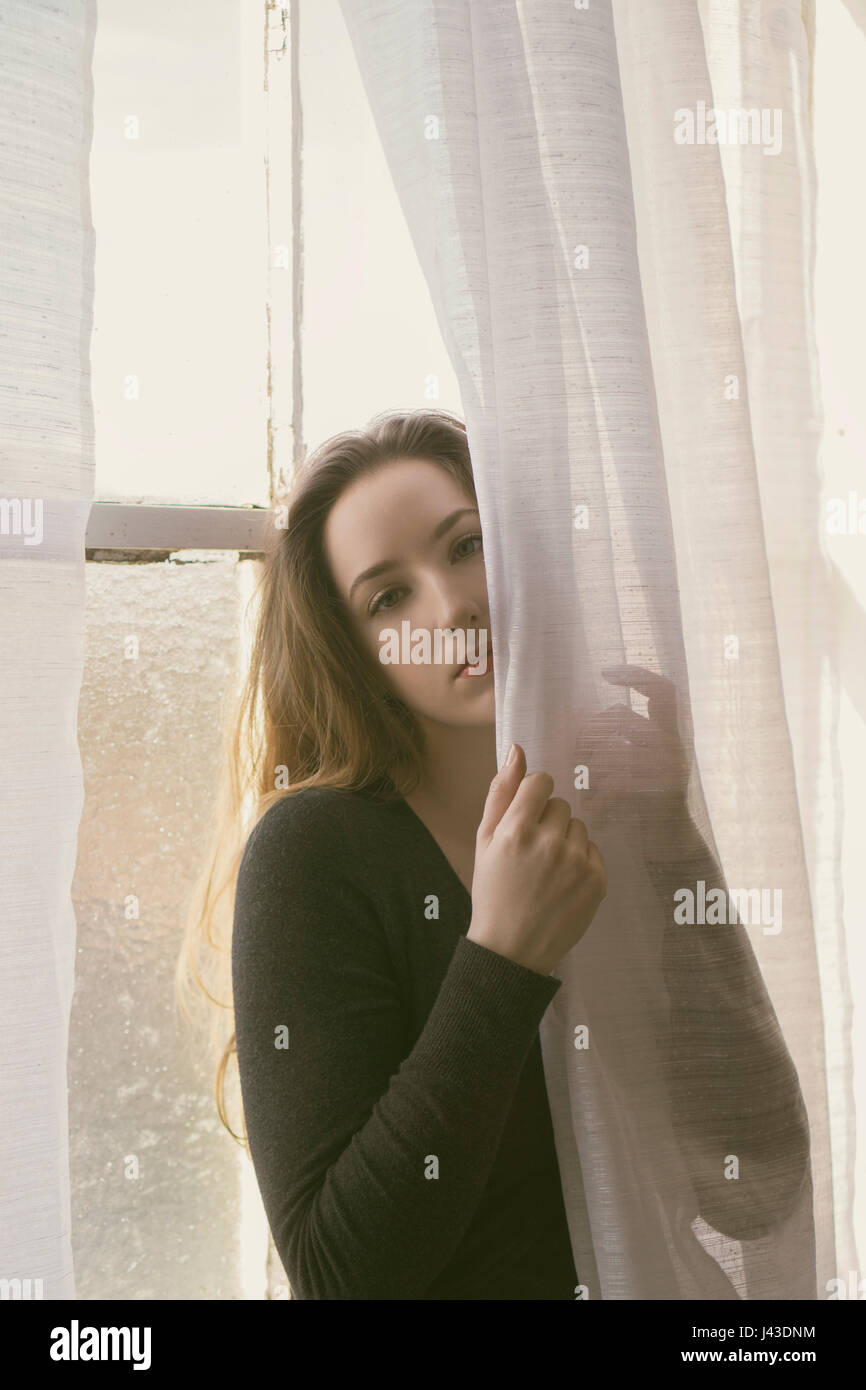 Beautiful young woman standing by the window Stock Photo