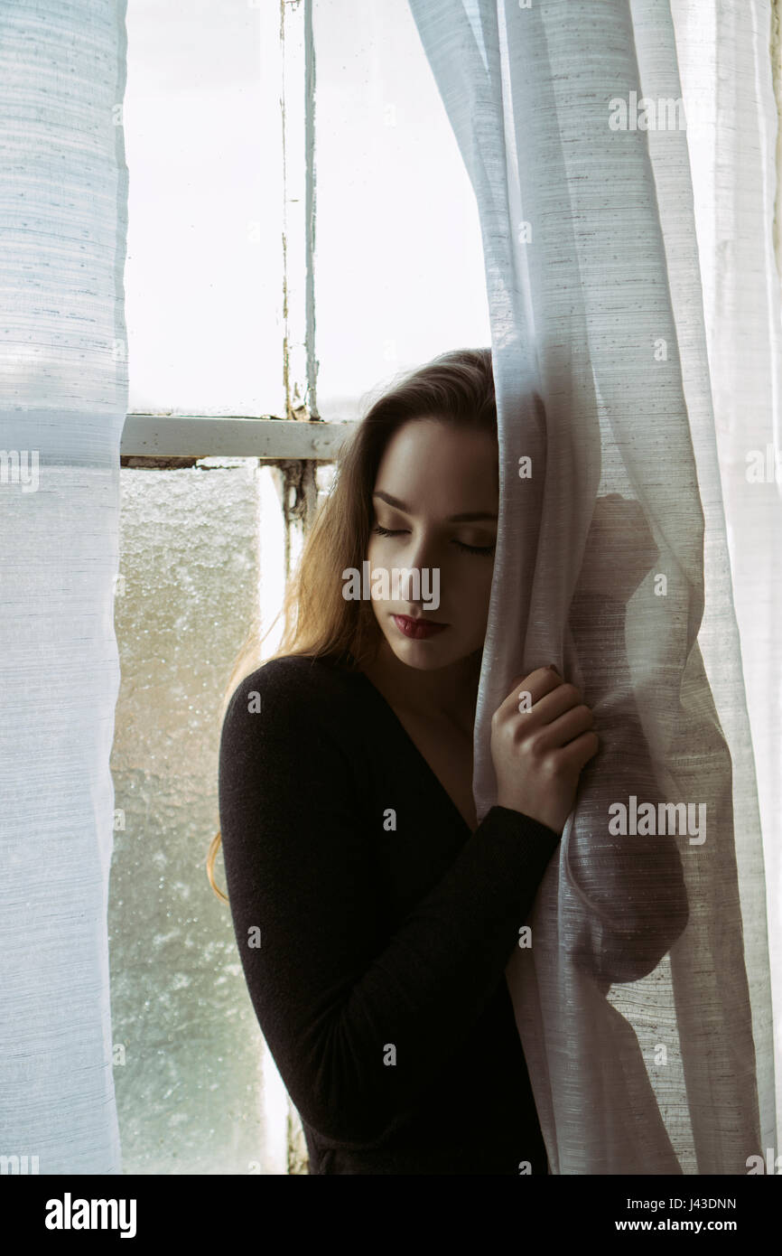 Sad young woman hands on the blinds by the window Stock Photo