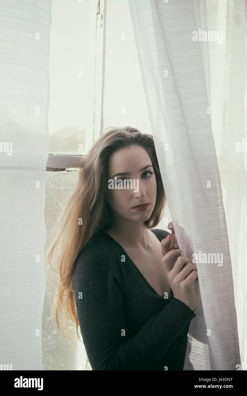 Beautiful young woman standing by the window Stock Photo