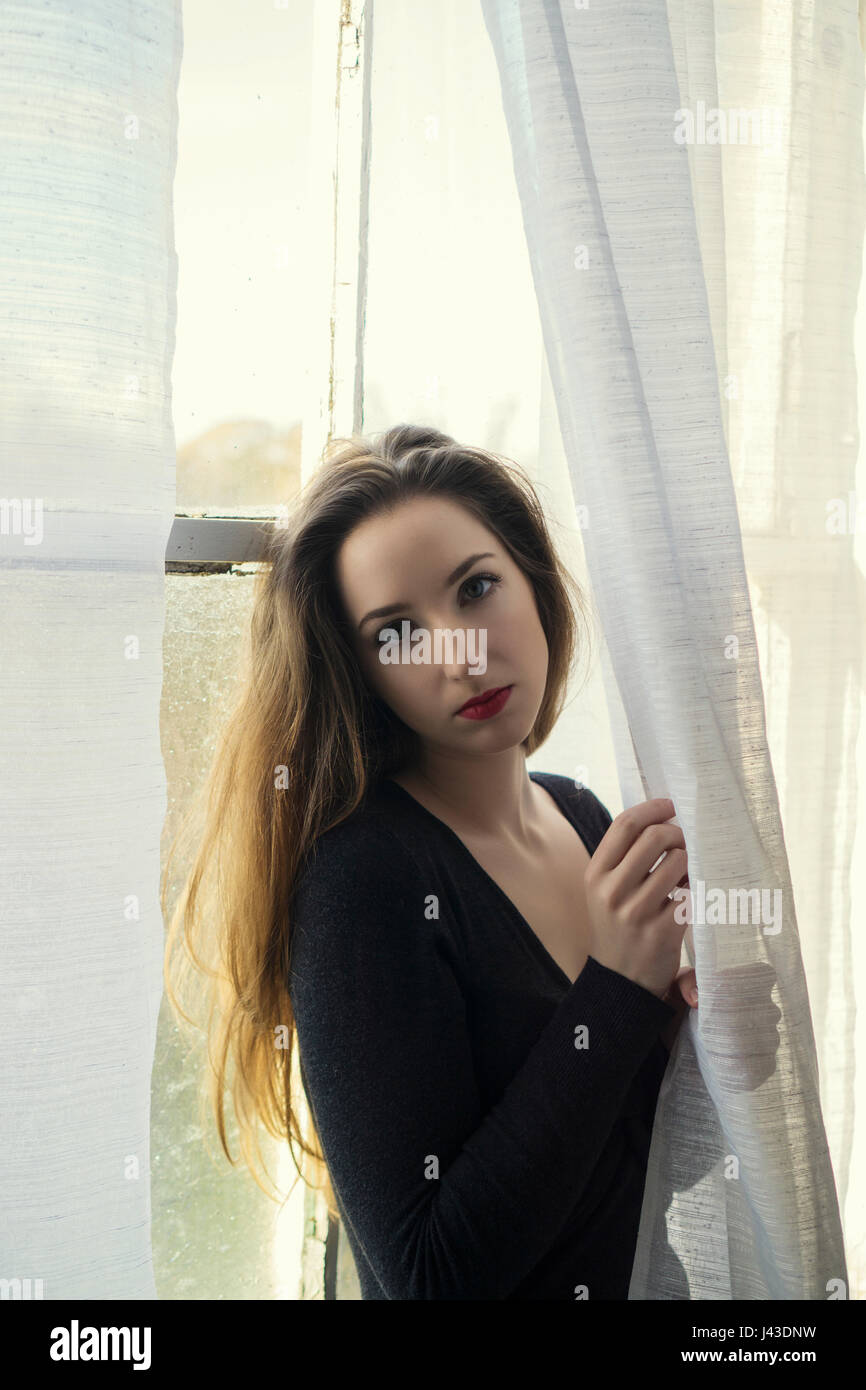 Beautiful young woman standing by the window Stock Photo