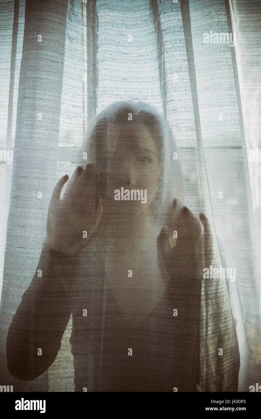 Sad young woman hands on the blinds by the window Stock Photo