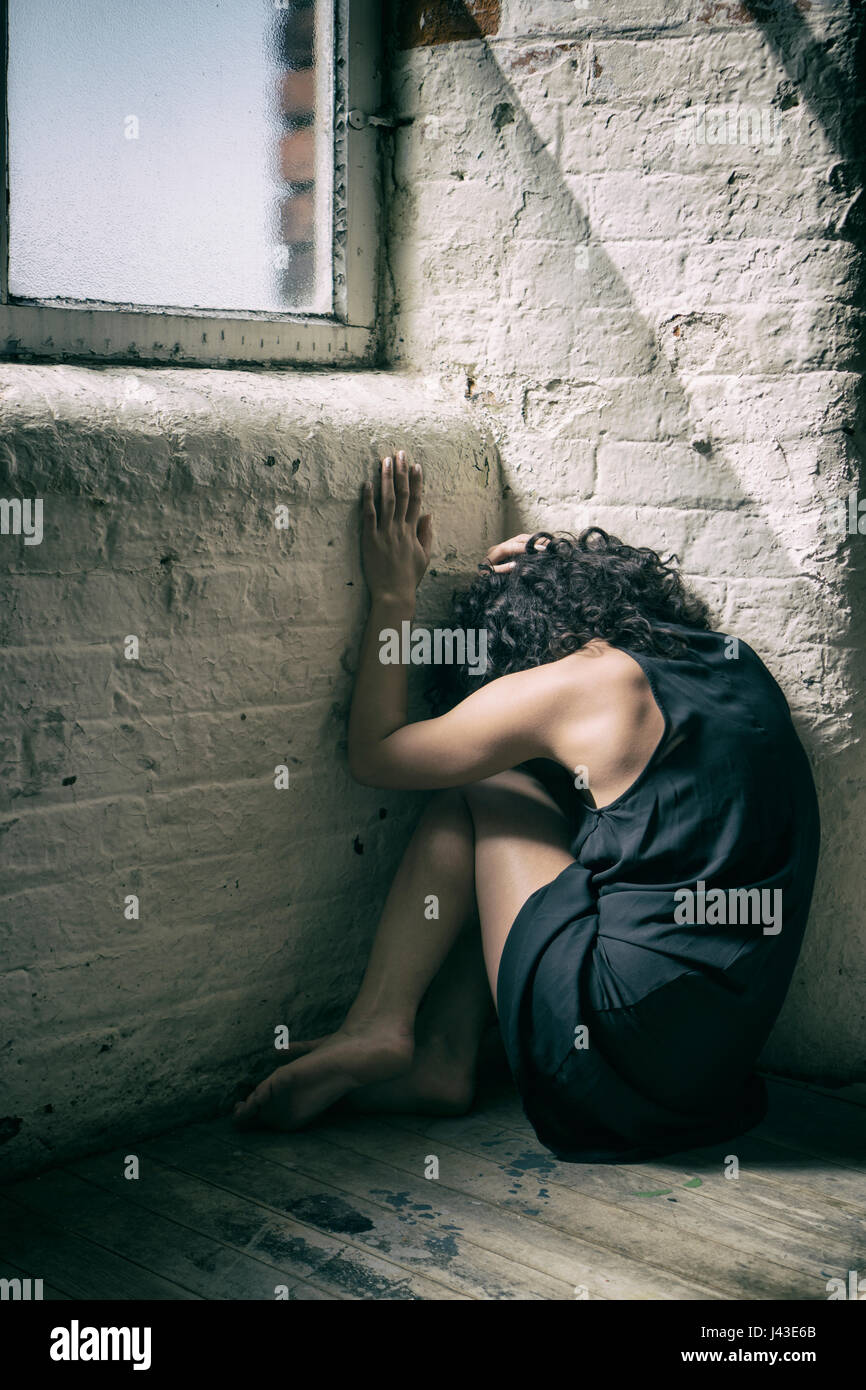 Rear view of a miserable young woman sitting on the floor by the window ...