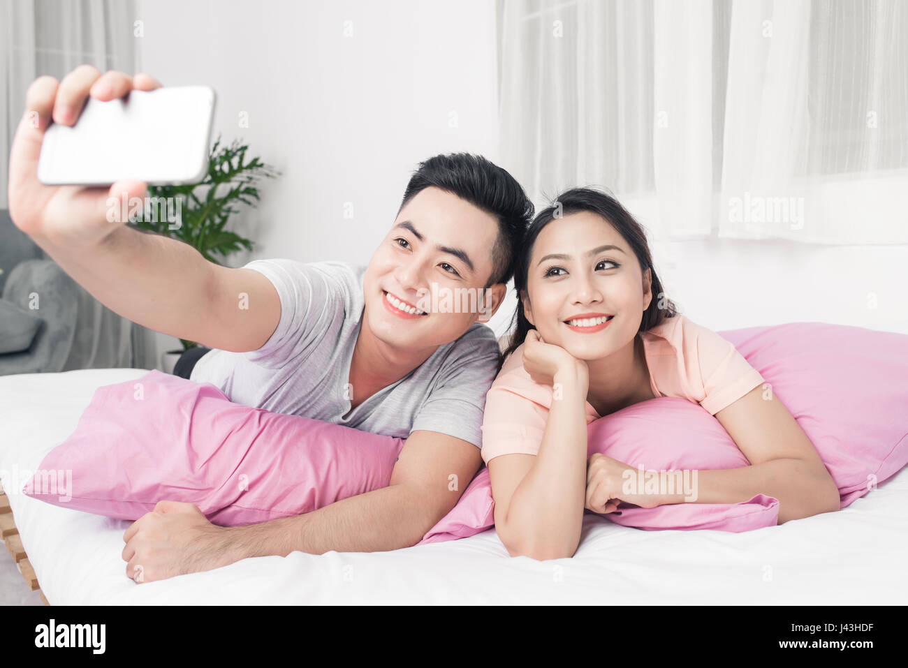 Couple taking selfie with phone lying on bed. Stock Photo