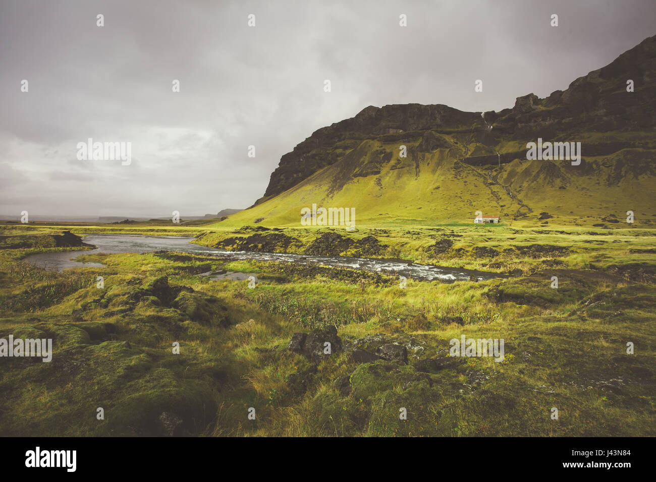 Cold water in Iceland. Stream in rocky mountains and lake side. Fresh and green grass. Beautiful mountain range in the background. Stock Photo