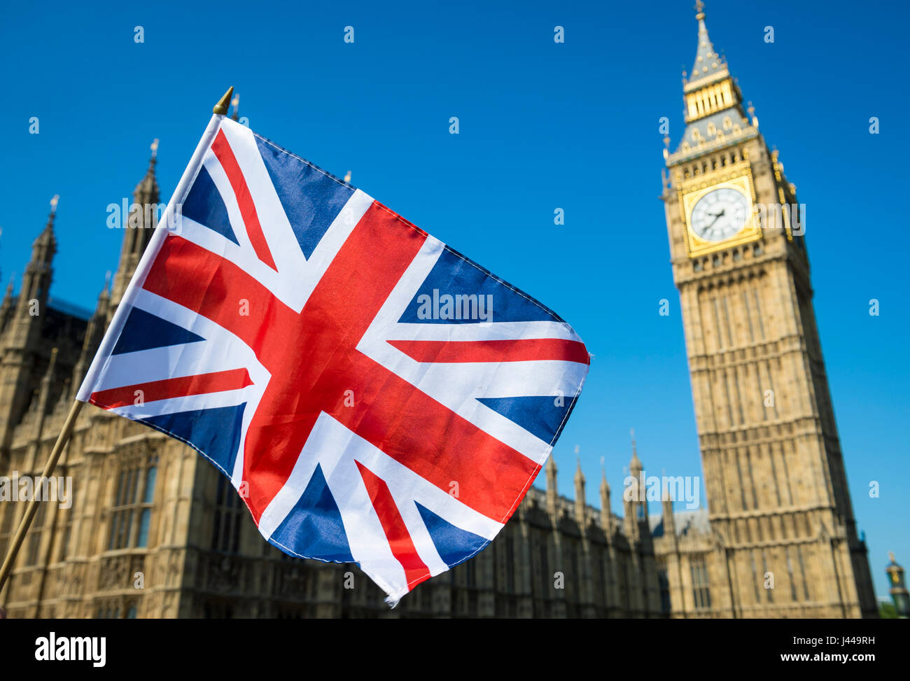 United Kingdom flag waving in bright blue sky in front of the Houses of Parliament at Westminster Palace with Big Ben Stock Photo