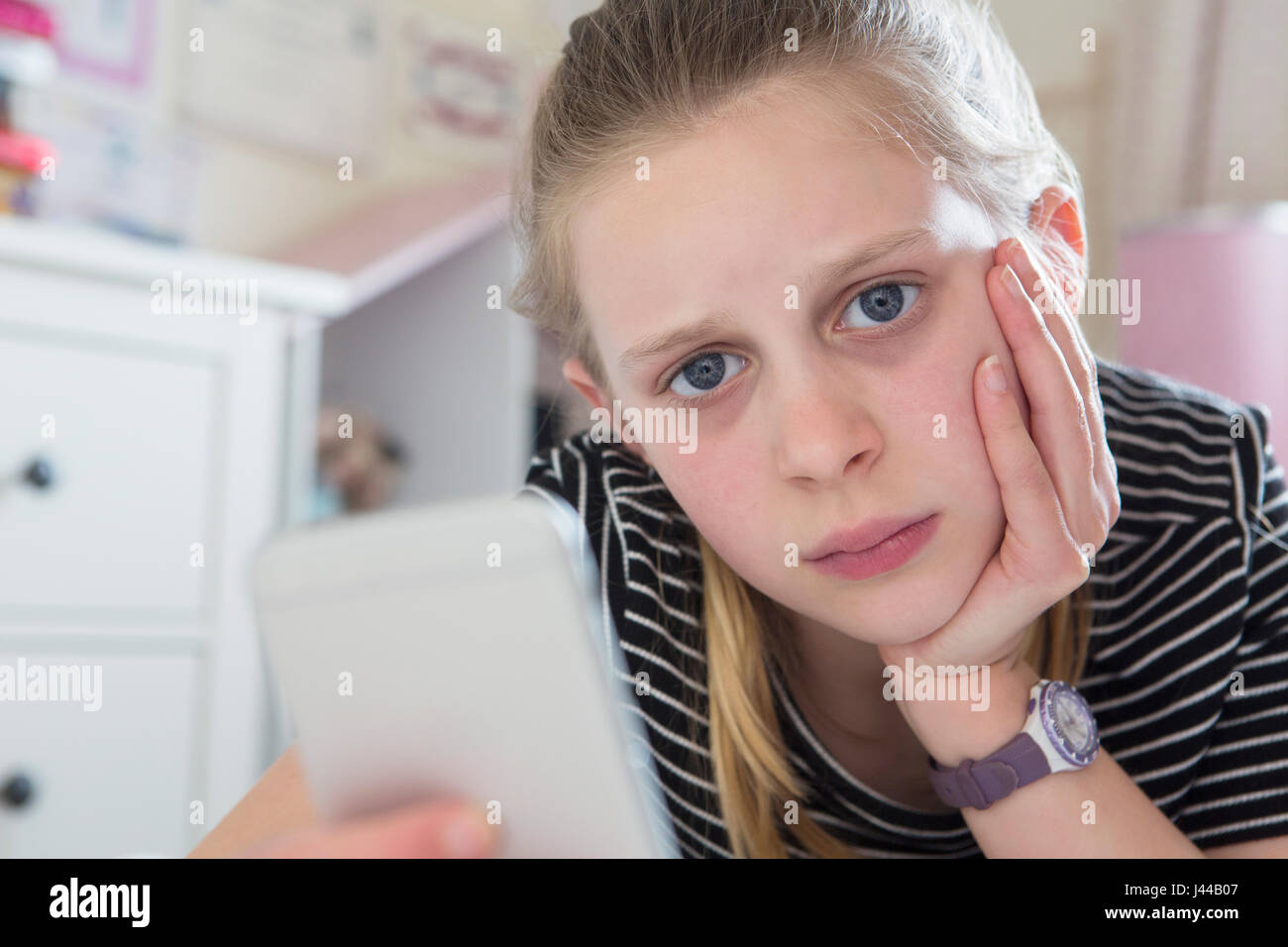 Young Girl Victim Of Bullying By Text Message Lying On Bed At Home Stock Photo
