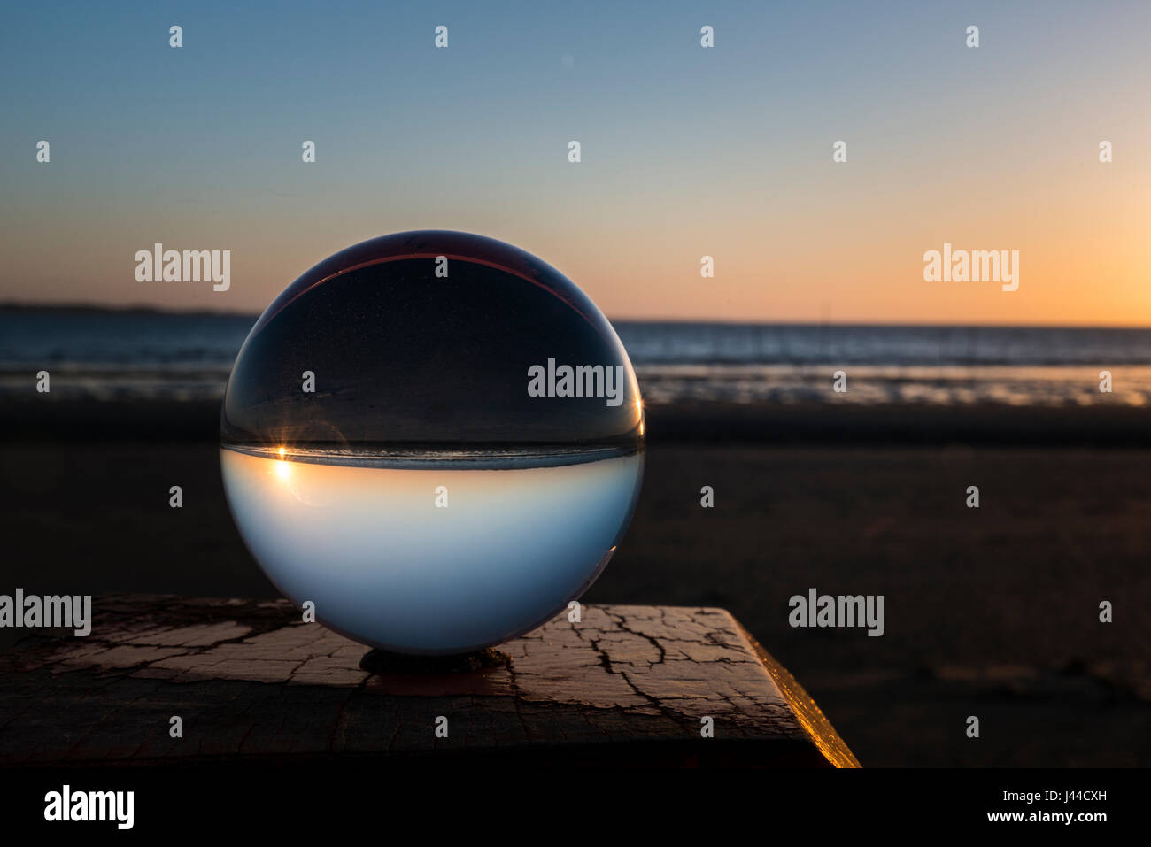 sunset on the beach on wooden pole captured in glass crystal sphere Stock Photo