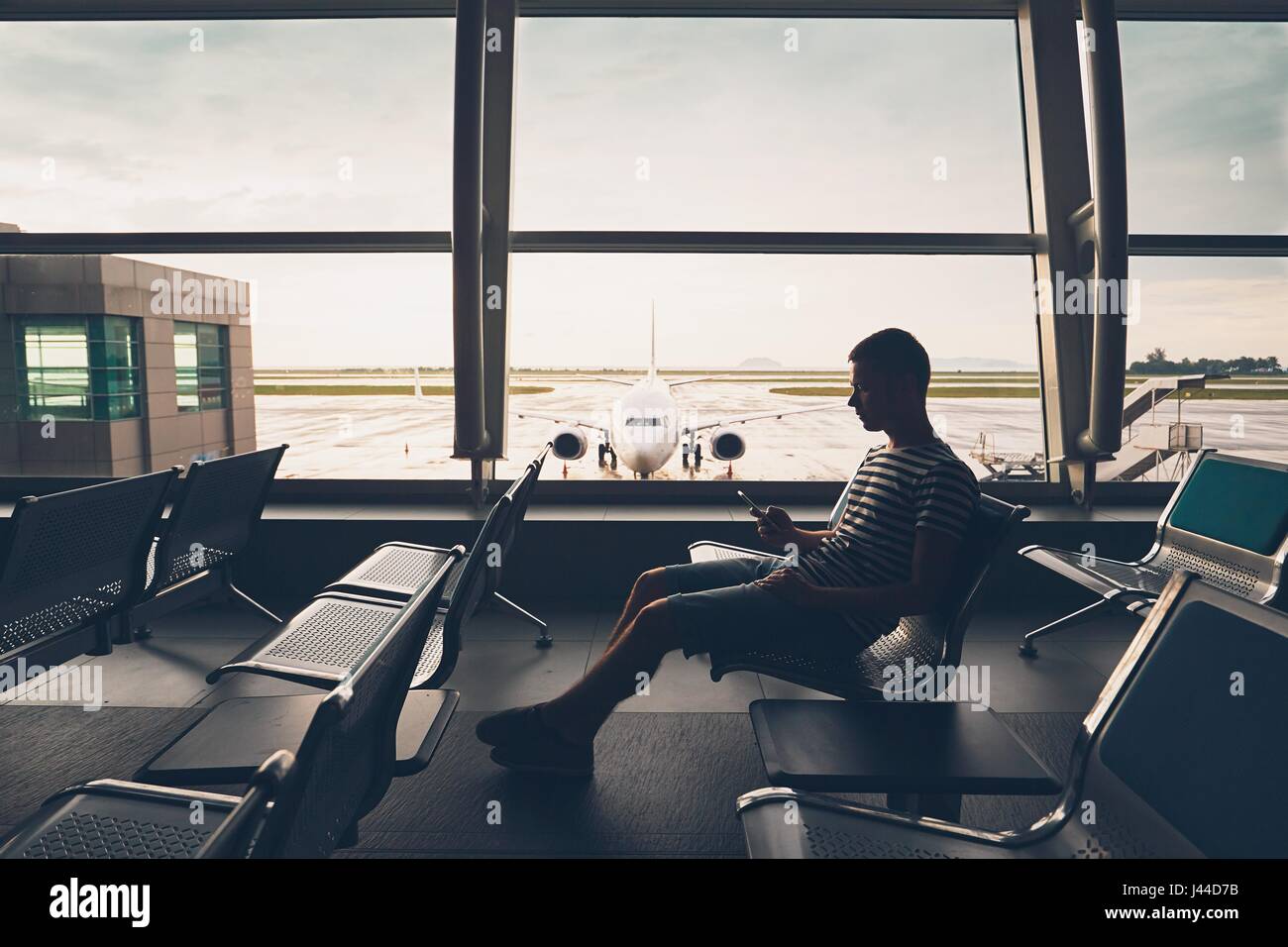 Silhouette of the traveler inside airport terminal. Young man using mobile phone and waiting for his flight. Stock Photo