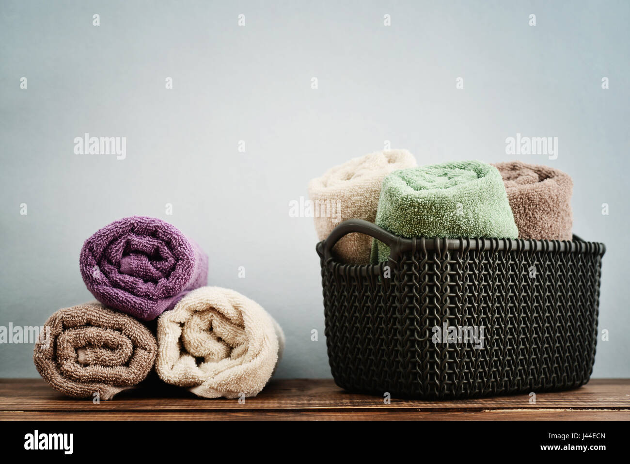 Bath towels of different colors in wicker basket on light background