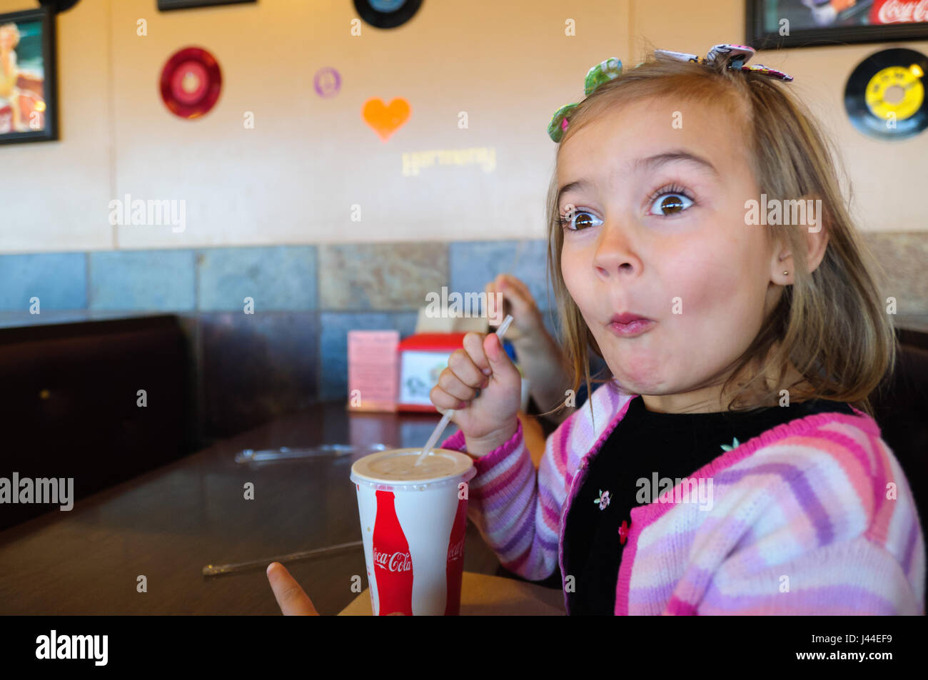 Girl sitting in a diner drinking her soda and making a funny face. Stock Photo