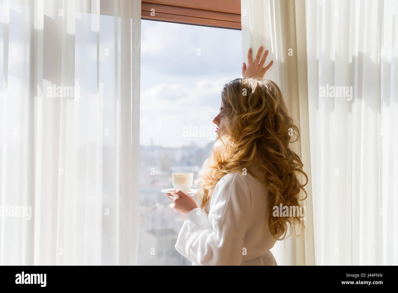 Beautiful woman in sheer nightgown looking out of a window with  backlighting Stock Photo - Alamy