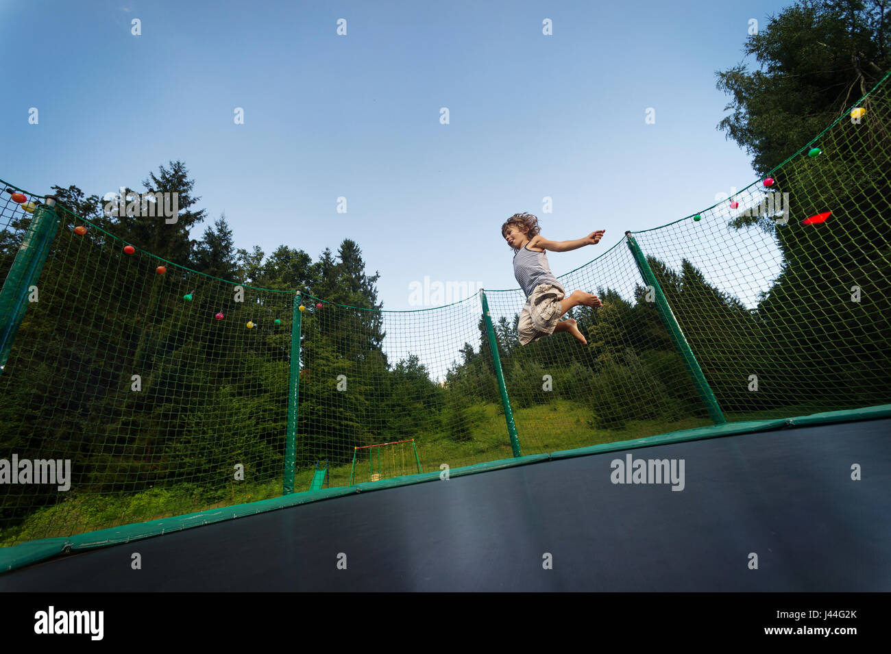 Cute boy enjoys jumping and bouncing on trampoline oudoors. Stock Photo