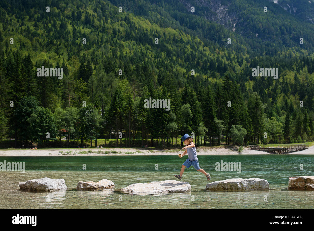 Adorable young boy with a hat crossing river or water jumping from rock to rock. Crossing the gap, freedom, liberation, success, avoiding danger, cour Stock Photo