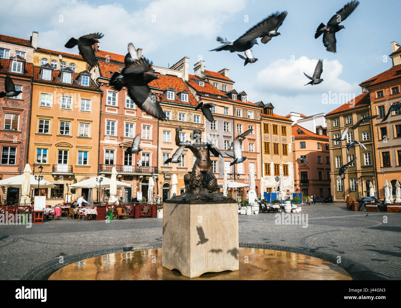 Birds of pigeons are flying through Stare Miasto Old Town Market Square with Mermaid Syrena Statue in the center of Warsaw, Poland. Stock Photo