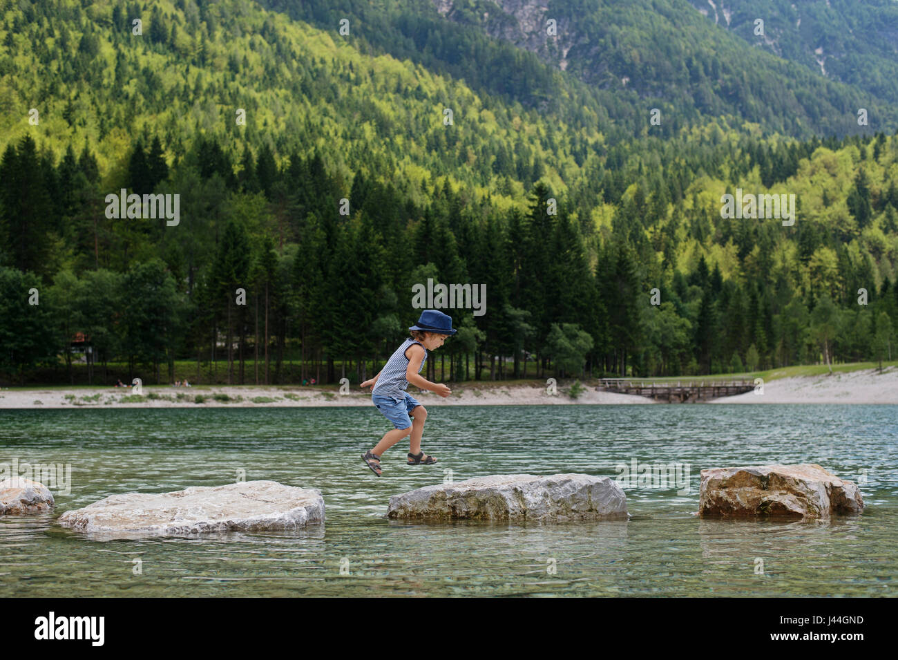 Adorable young boy with a hat crossing river or water jumping from rock to rock. Crossing the gap, freedom, liberation, success, avoiding danger, cour Stock Photo