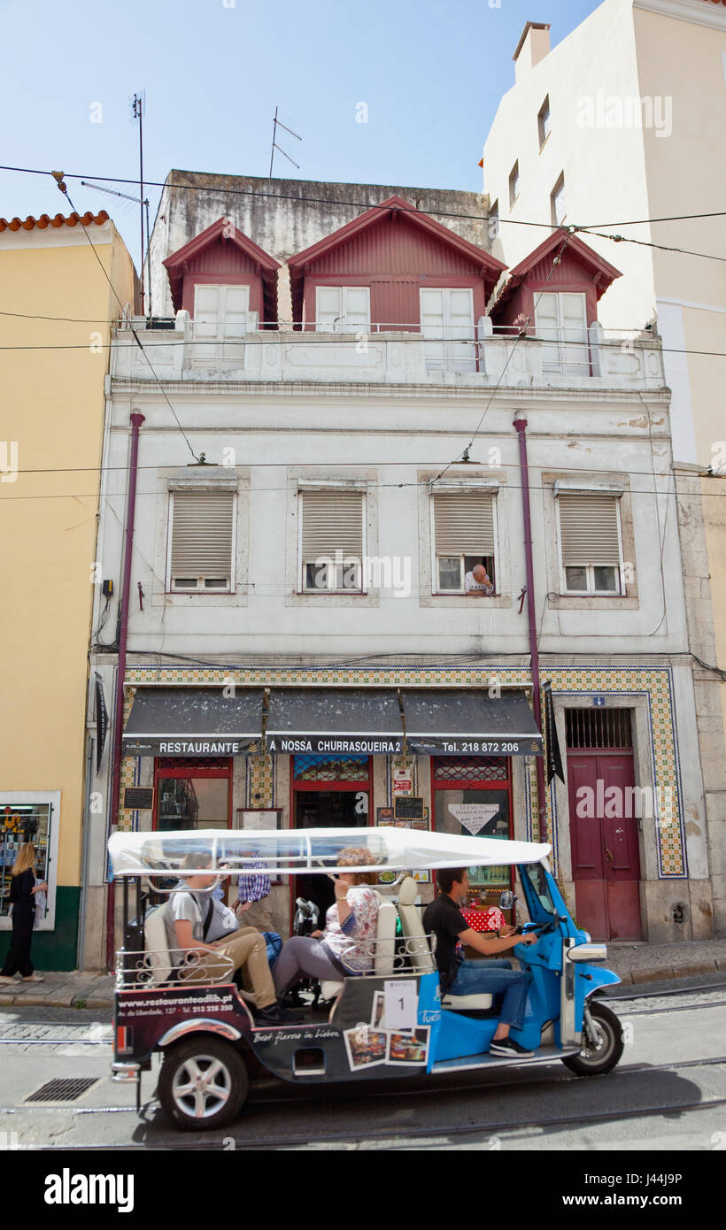 Portugal, Estremadura, Lisbon, Alfama district, Tuk Tuk full of tourist passing cafe. Stock Photo