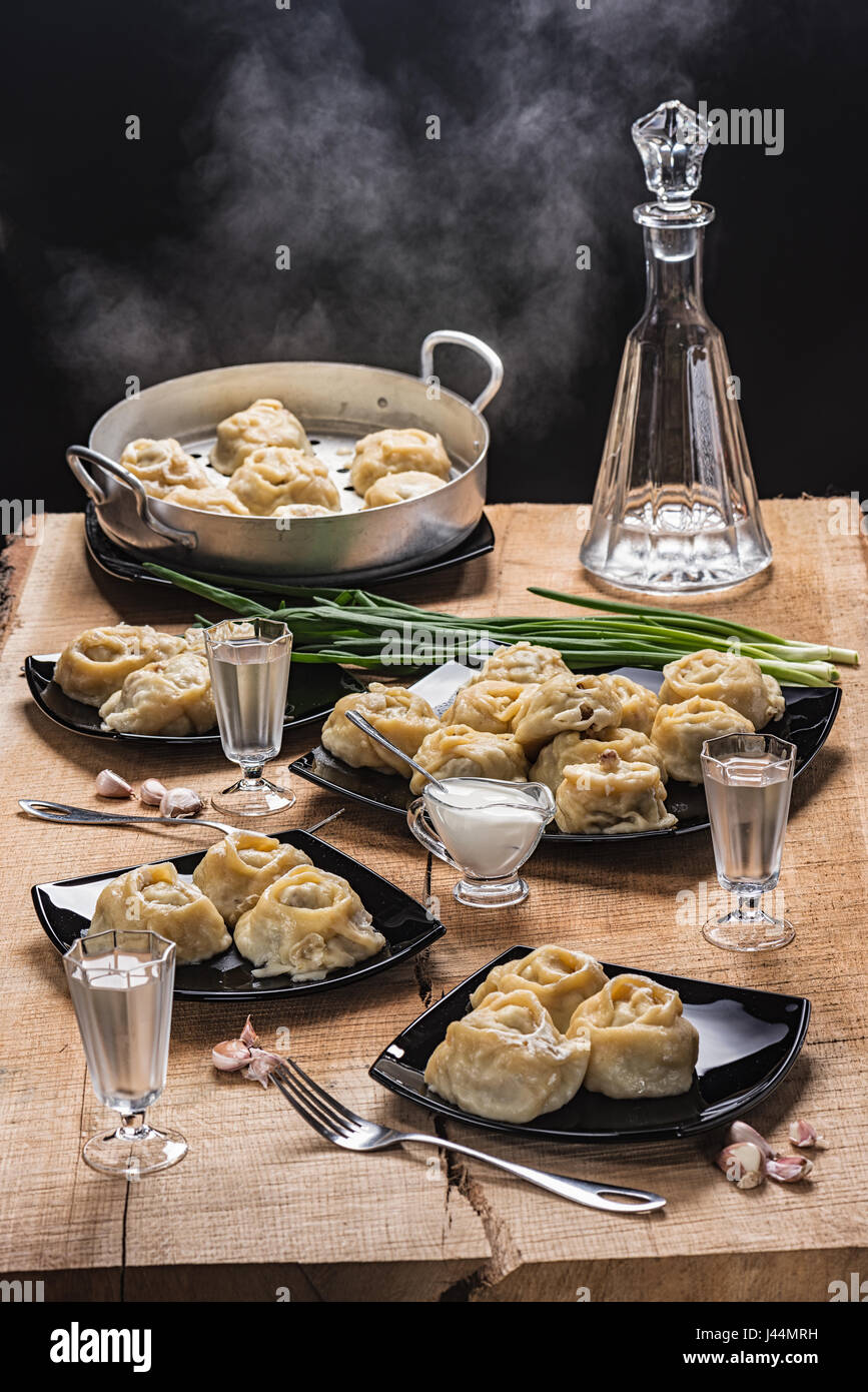 Ready hot manti on black plates, vodka in the countess and three piles on an oak table-top Stock Photo