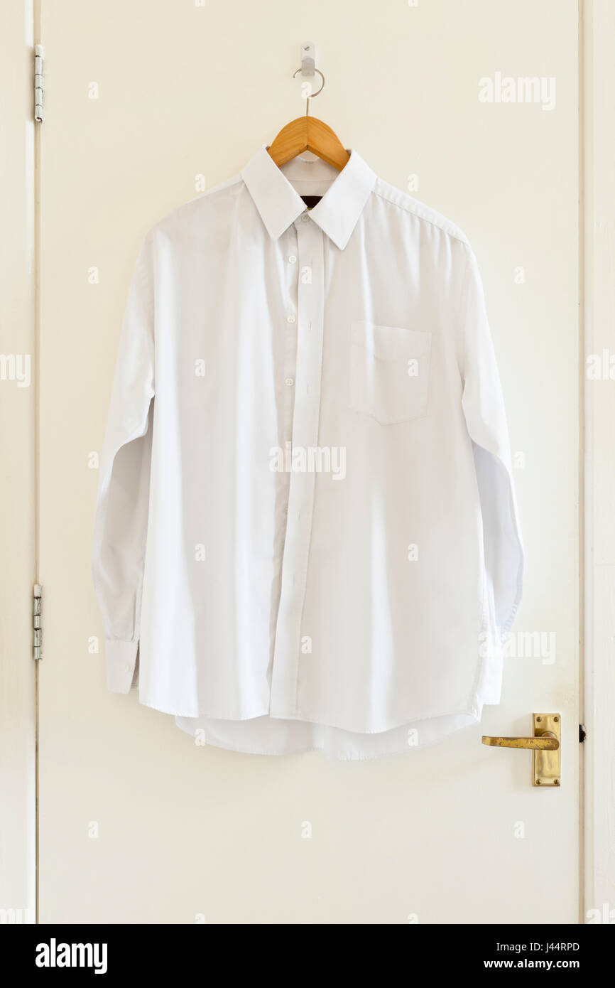 White shirt on a clothes hanger hanging on the back of a door Stock Photo