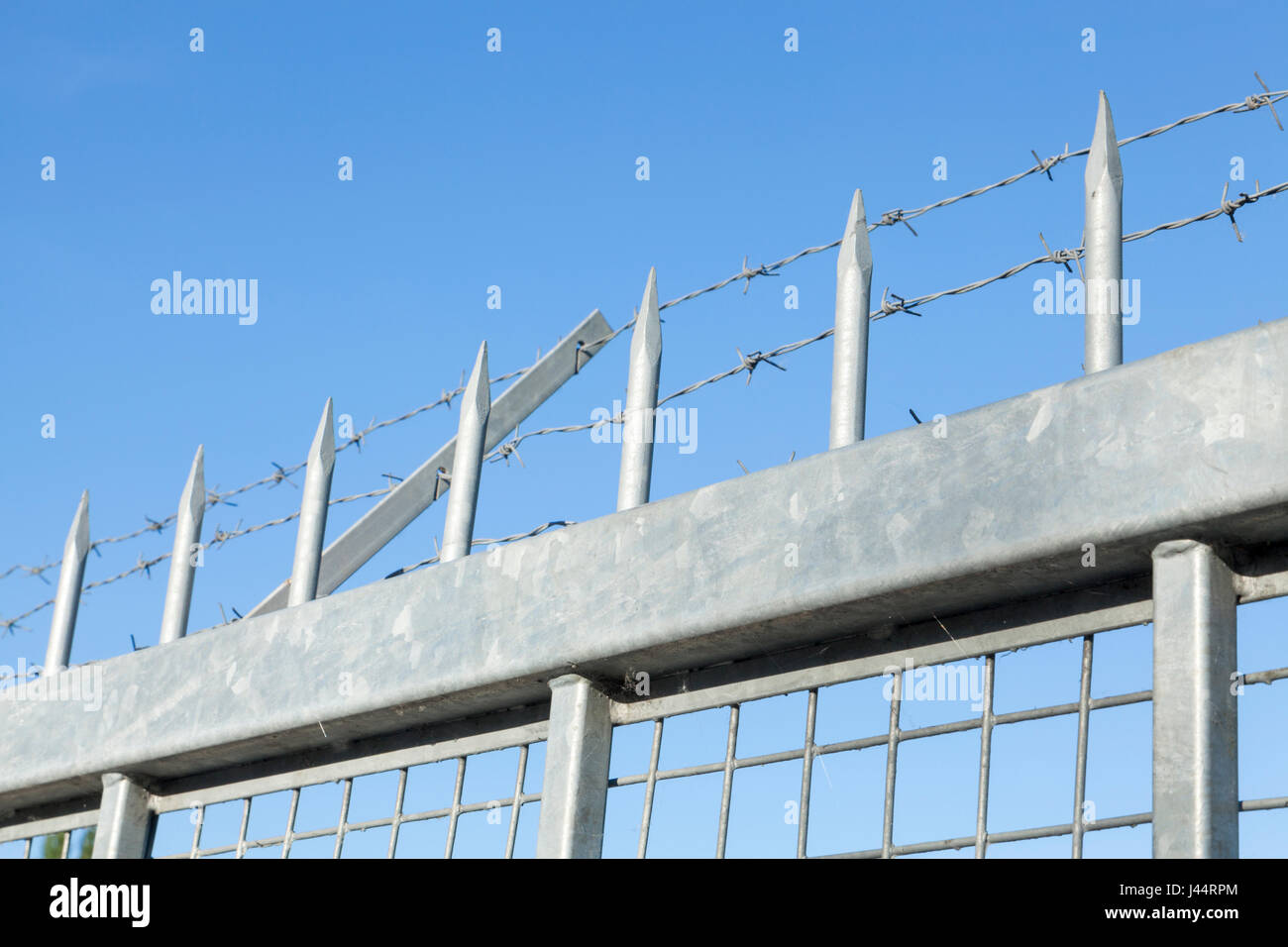 Security fencing with spikes and barbed wire against a blue sky, England, UK Stock Photo