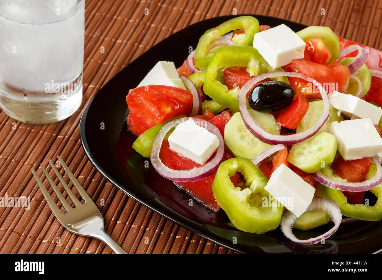 Glass of ouzo drink and fresh salad with green pepper and red onion rings, tomatoes, cucumber and cottage cheese. Traditional balkan food starter Stock Photo