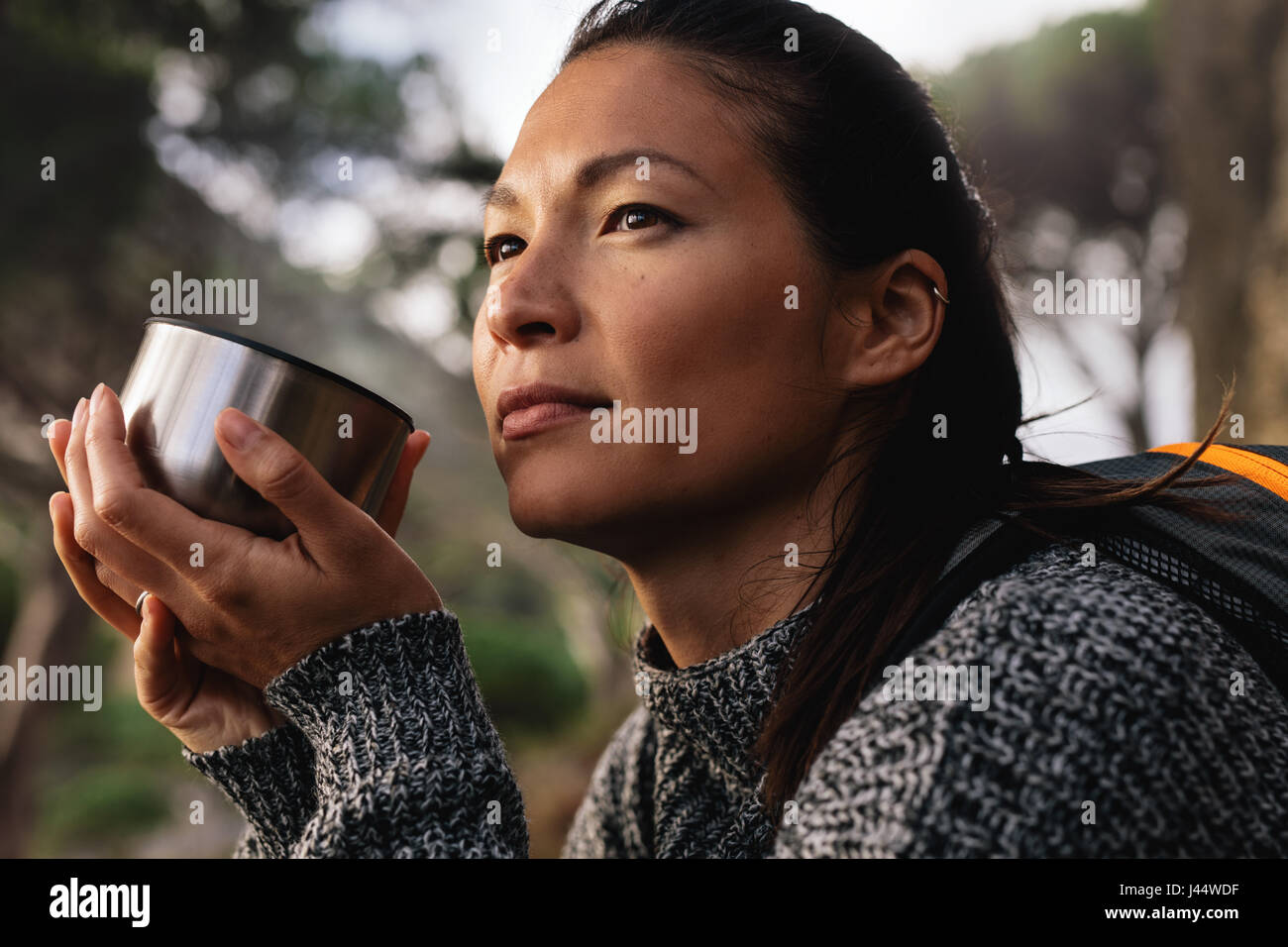 Close up side shot of female hiker resting outdoors with a coffee and looking away. Asian woman having coffee. Stock Photo