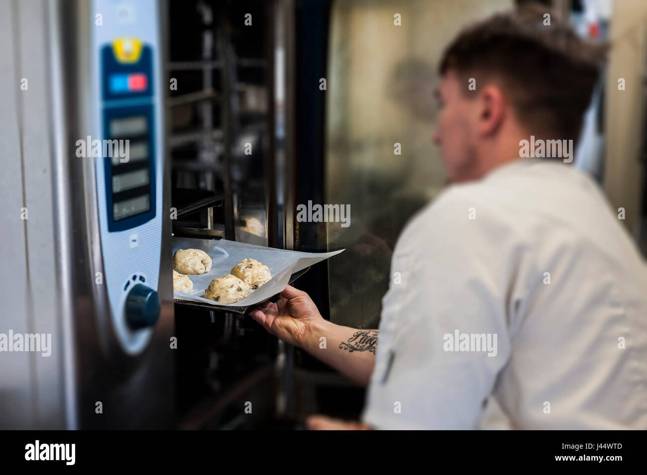 A chef puts a tray of scones into an oven; Kitchen; Food; Cooking; Baking; Restaurant; Food preparation; Food service industry; Worker; Working; Pract Stock Photo