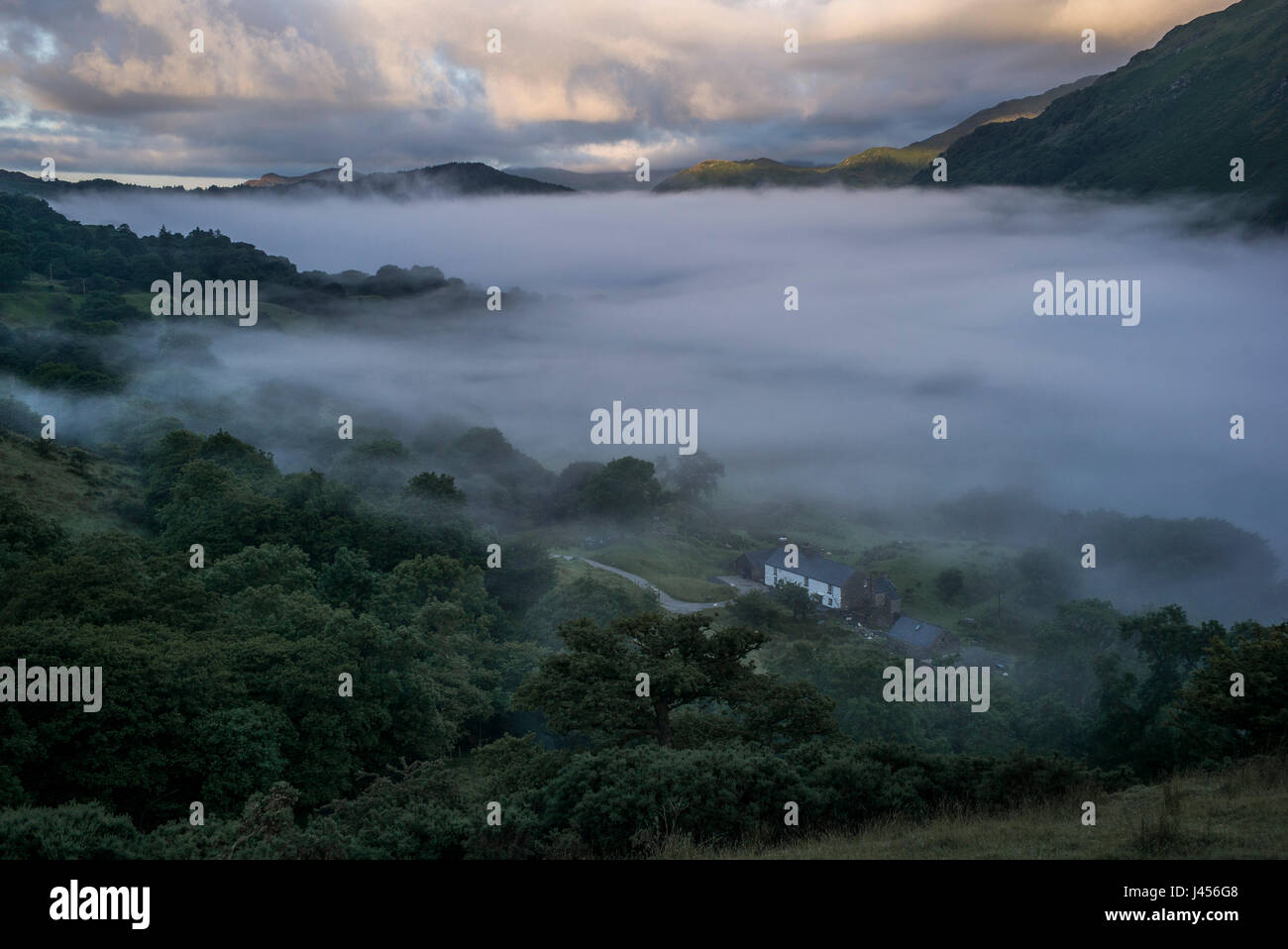 A farmhouse appears from under a low lying cloud of mist in a valley in Snowdonia National Park, Wales, UK. Stock Photo