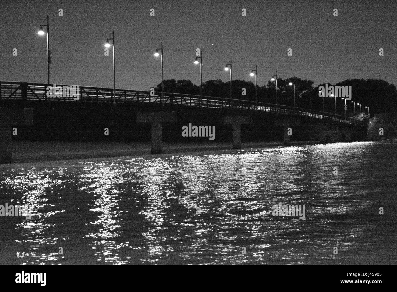 Grainy black and white photo of lights illuminating the Mockingbird footbridge at night at the northern end of White Rock Lake in Dallas, Texas Stock Photo