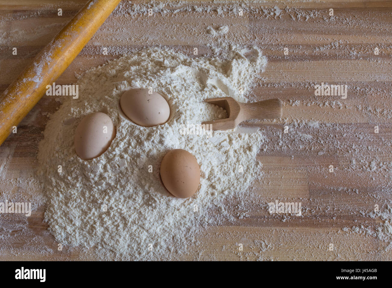 Bakery background. Flour, domestic eggs, wooden spoon for flour and a wooden rolling pin Stock Photo