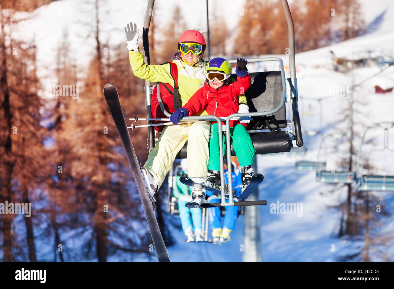 Happy skiers lifting on chairlift and waving hands Stock Photo