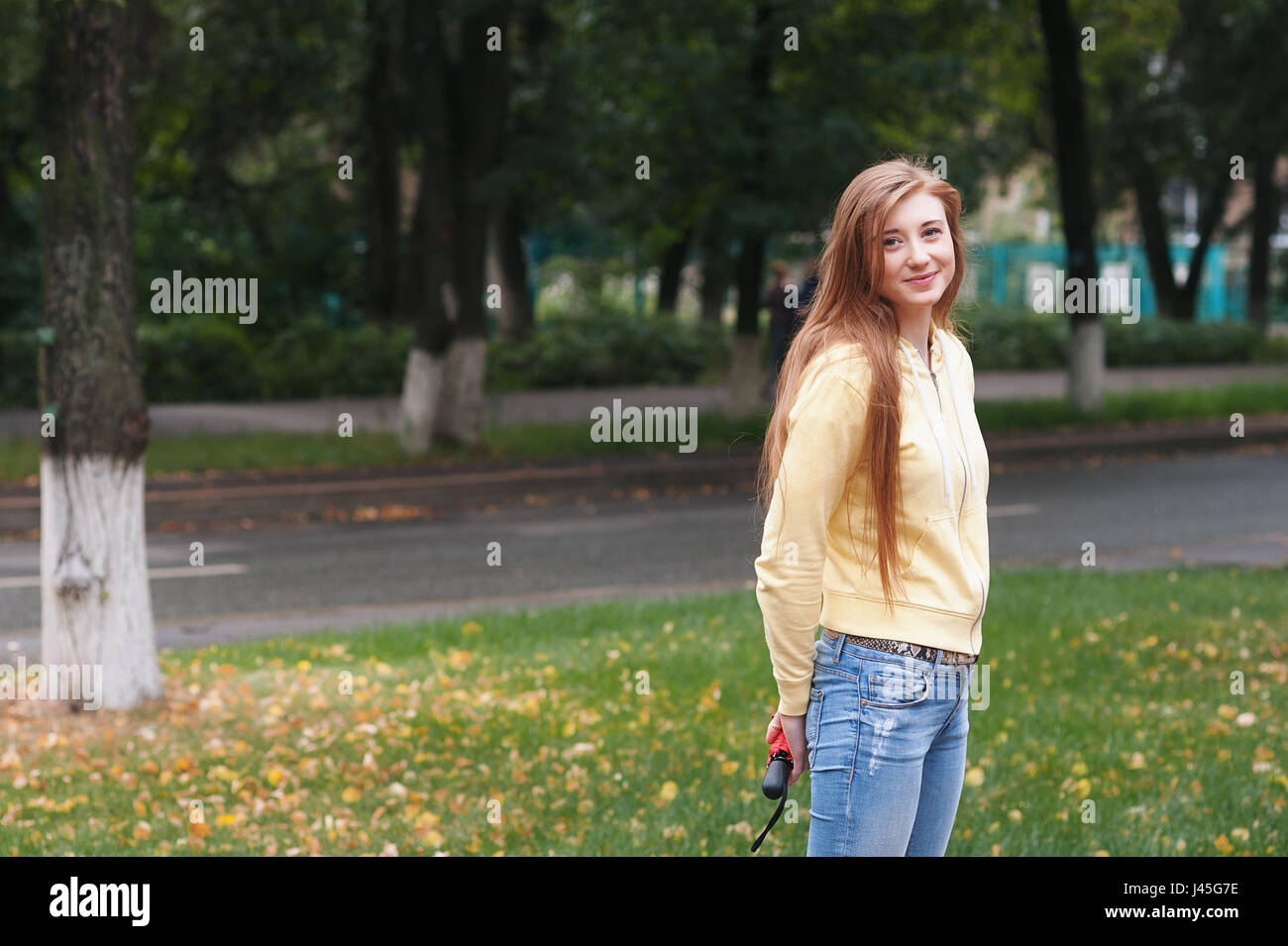 A pretty girl with long red hair, walks through the park and smiles ...