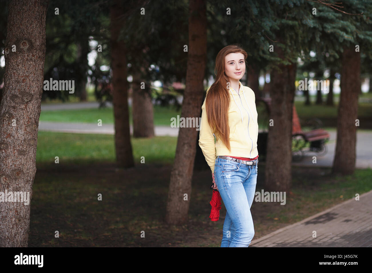 A pretty girl with long red hair, walks through the park and smiles ...
