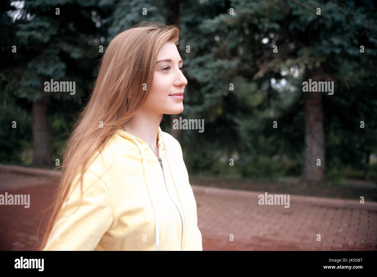 A pretty girl with long red hair, walks through the park and smiles ...