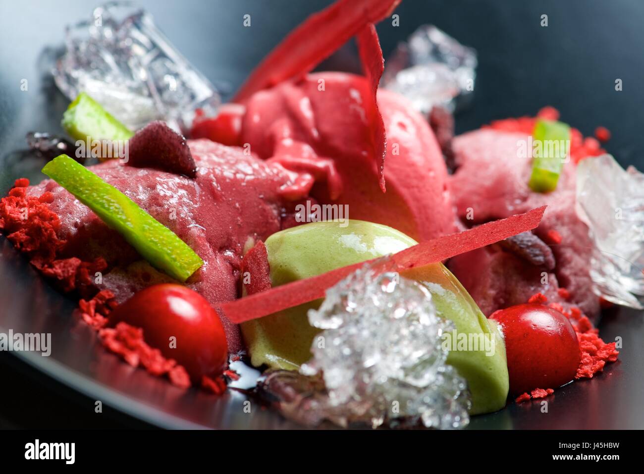Strawberry and pistachio ice cream with cherries in a black bowl Stock