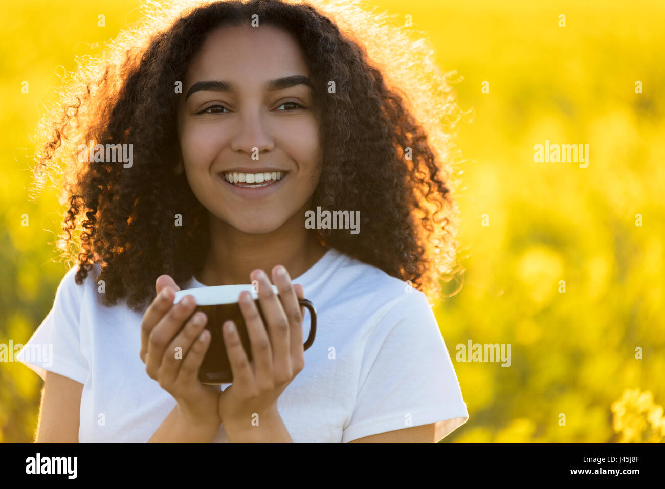 Beautiful happy mixed race African American girl teenager female young woman smiling drinking coffee or tea outdoors Stock Photo