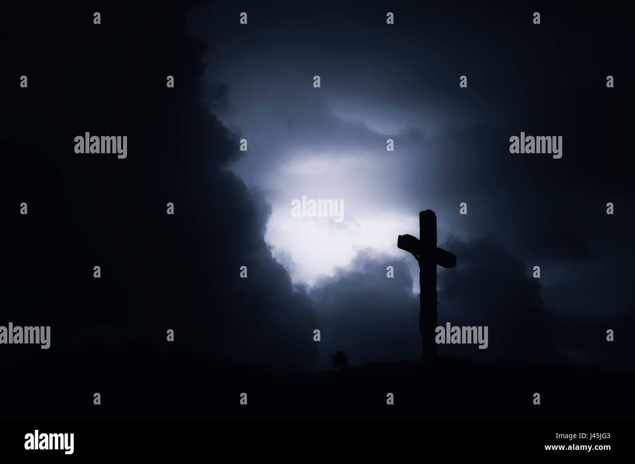 dark scary landscape with cross silhouette on hill with storm clouds at night Stock Photo