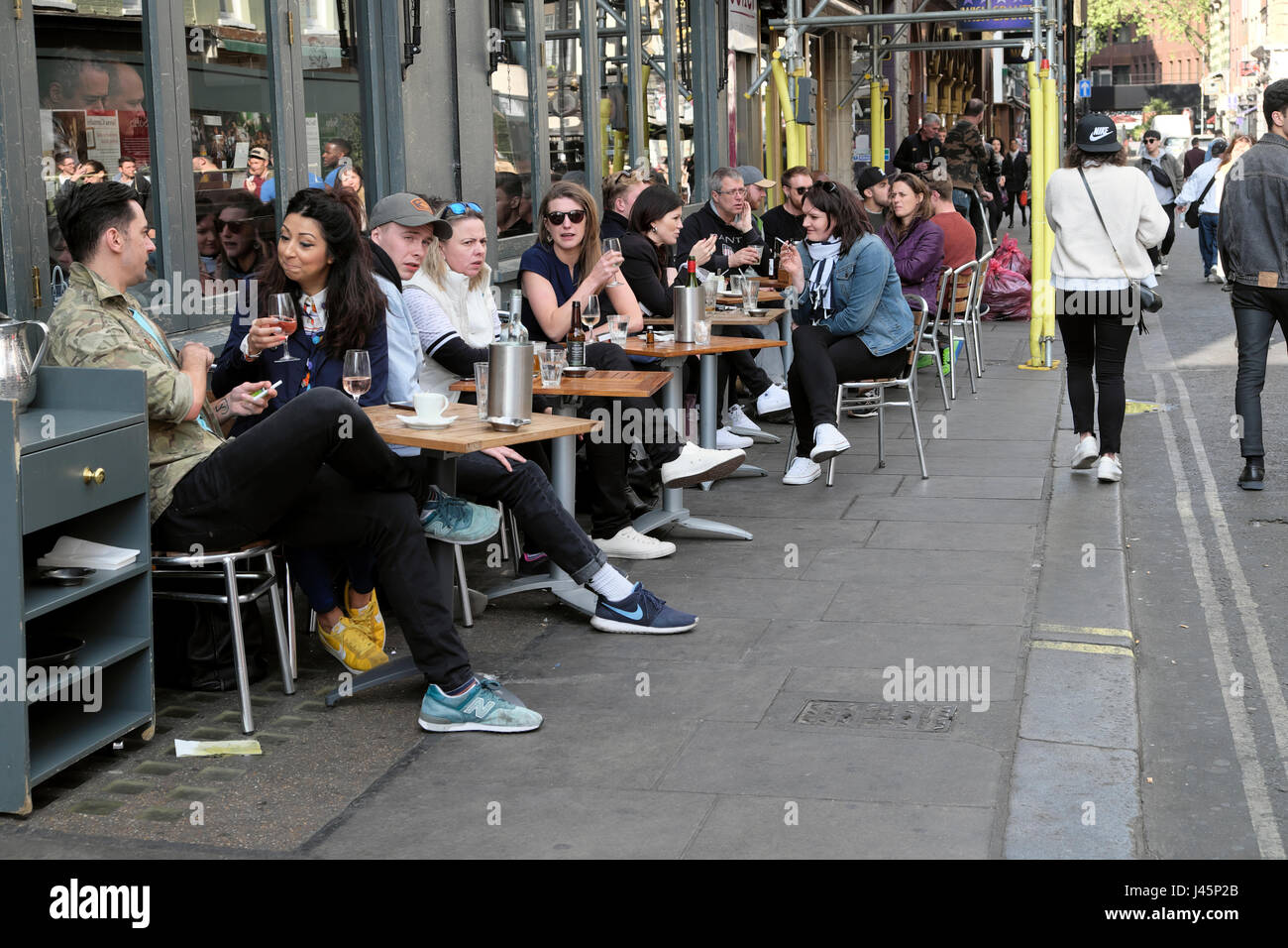 People drinking wine and beer sitting at tables relaxing outside a pub restaurant in spring on a street in Soho, London England UK    KATHY DEWITT Stock Photo