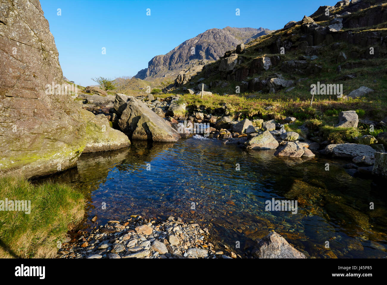 Crystal clear water of Afon Nant Peris in the Llanberis Pass with the formidable cliffs of Dinas Mot in the background with Crib Coch (red comb), a kn Stock Photo