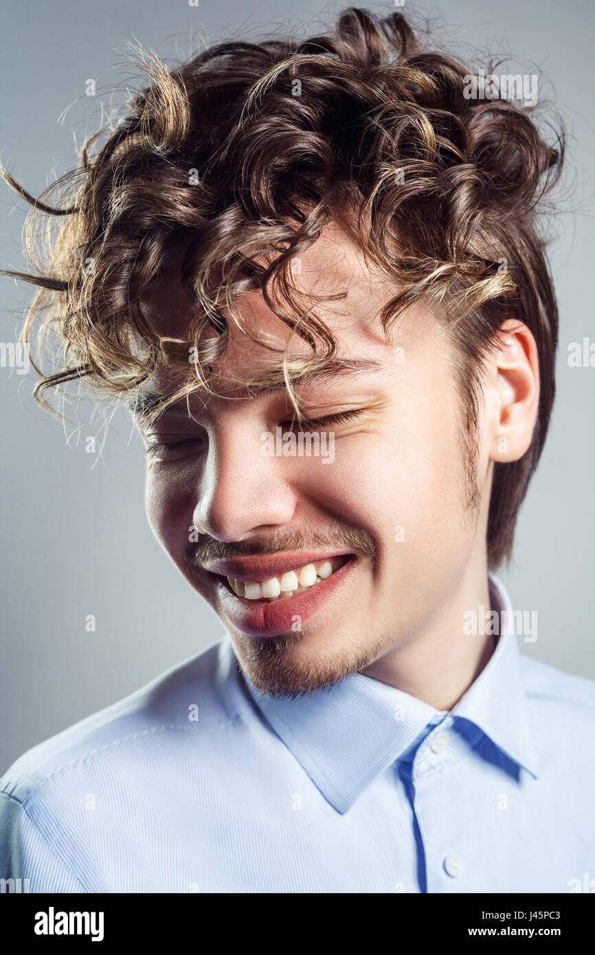 Portrait of young man with curly hairstyle. studio shot. toothy smile and closed eyes. Stock Photo