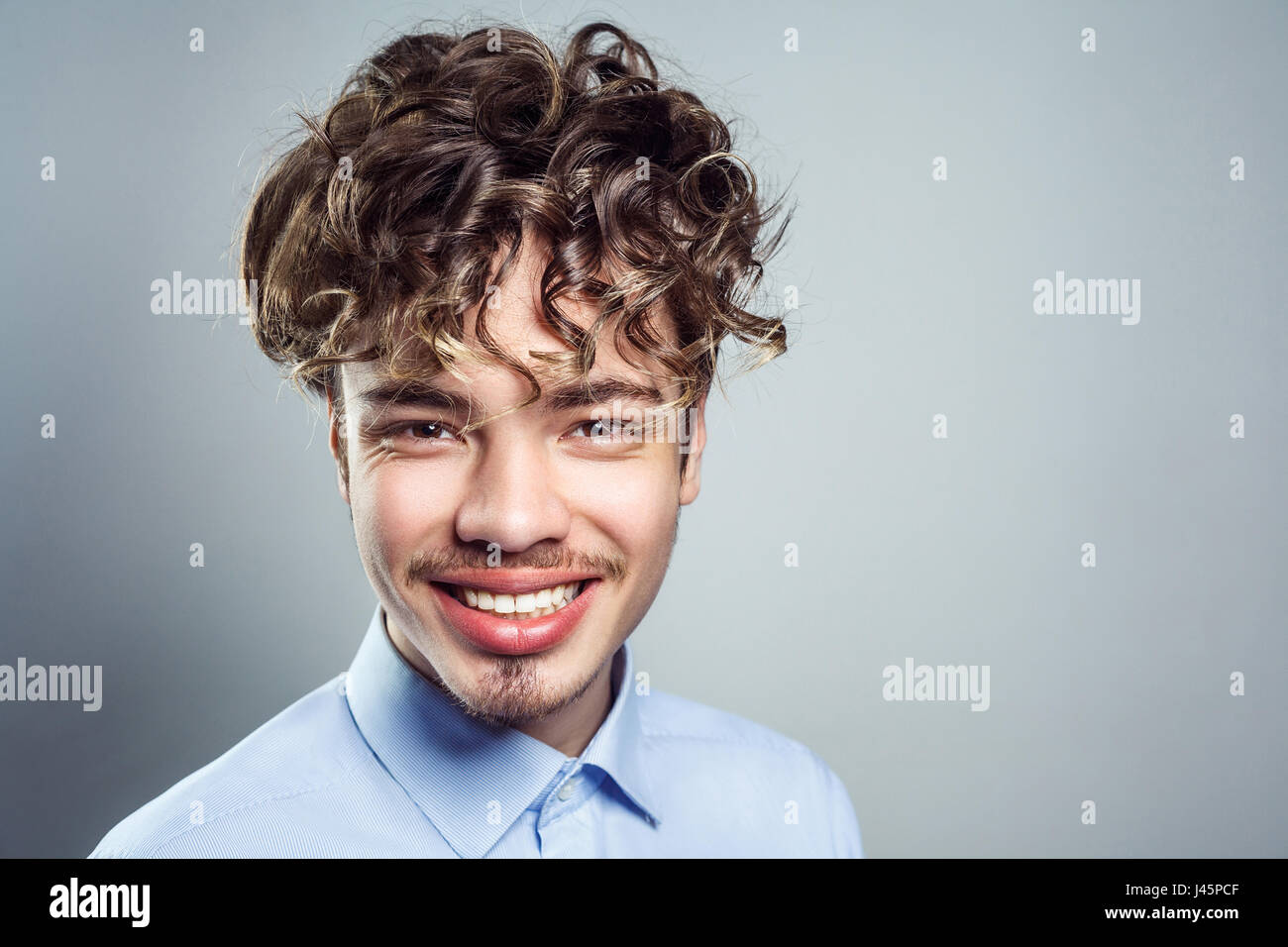 Portrait of young man with curly hairstyle. studio shot. looking at camera with toothy smile. Stock Photo