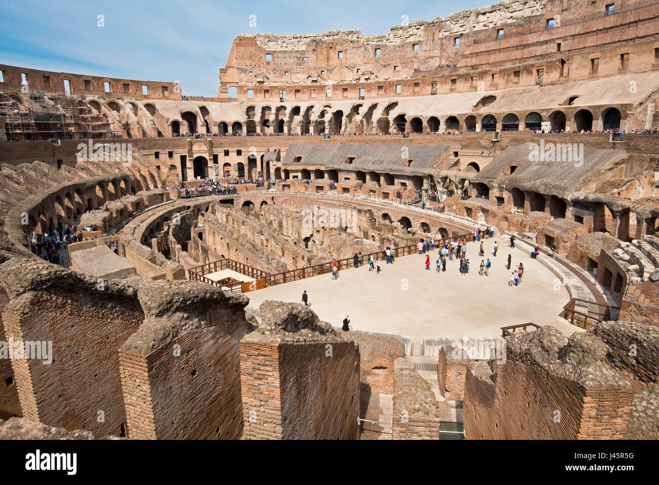 A wide angle interior view of the amphitheatre inside the Colosseum with tourists visitors on a sunny day with blue sky taken from the middle level 2. Stock Photo