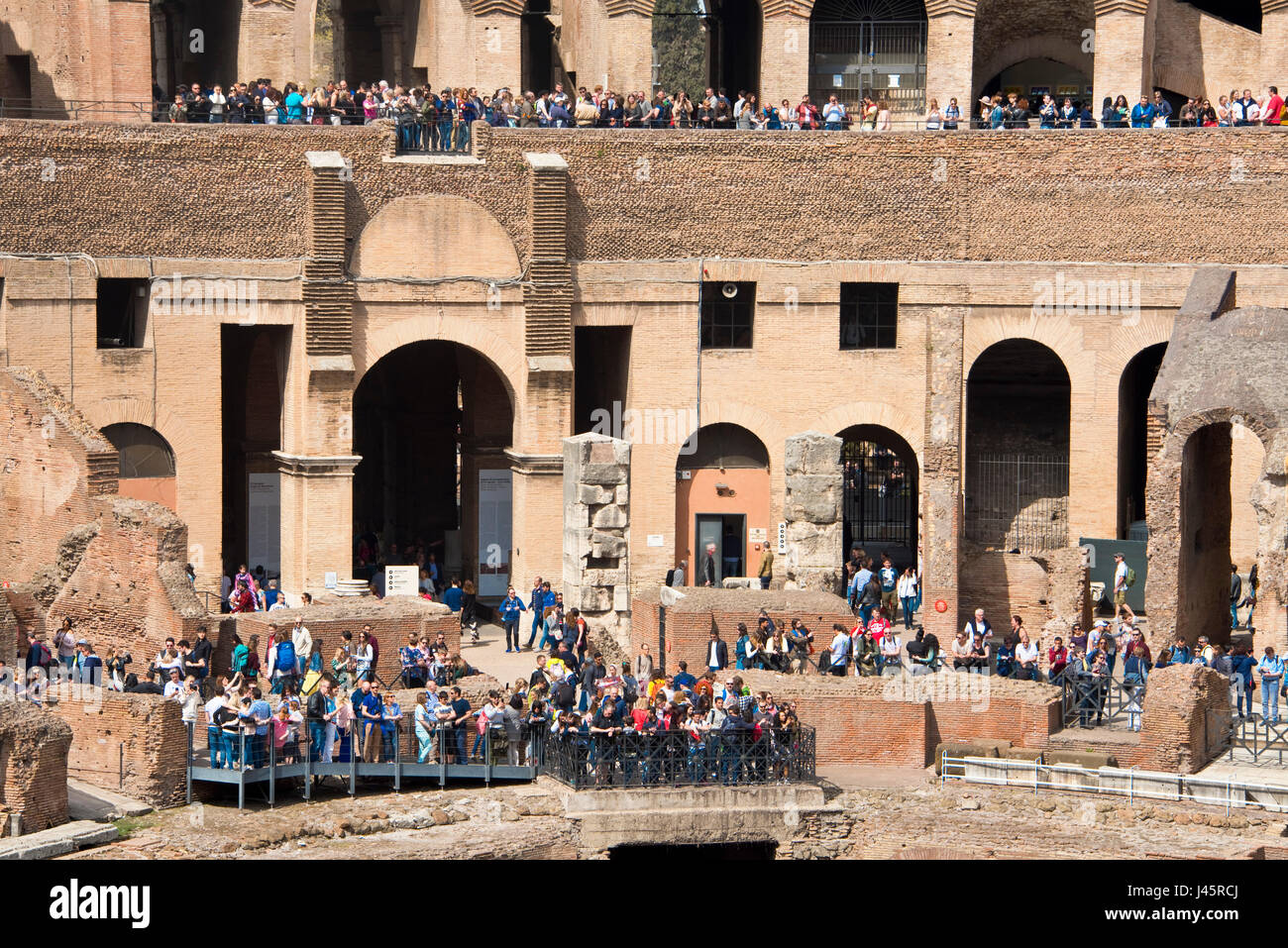 A compressed perspective interior view of the amphitheatre inside the Colosseum with tourists visitors on a sunny day taken from ground level. Stock Photo