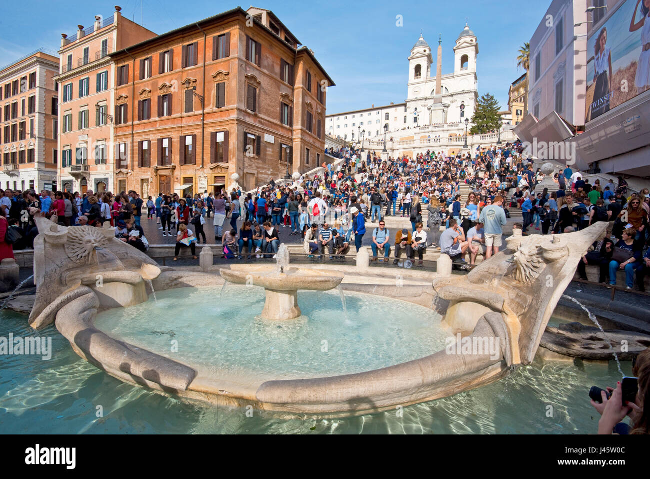 Spanish Steps in Rome with tourists on a sunny day with blue sky Trinità dei Monti church in the background and Fountain of the ugly Boat foreground. Stock Photo