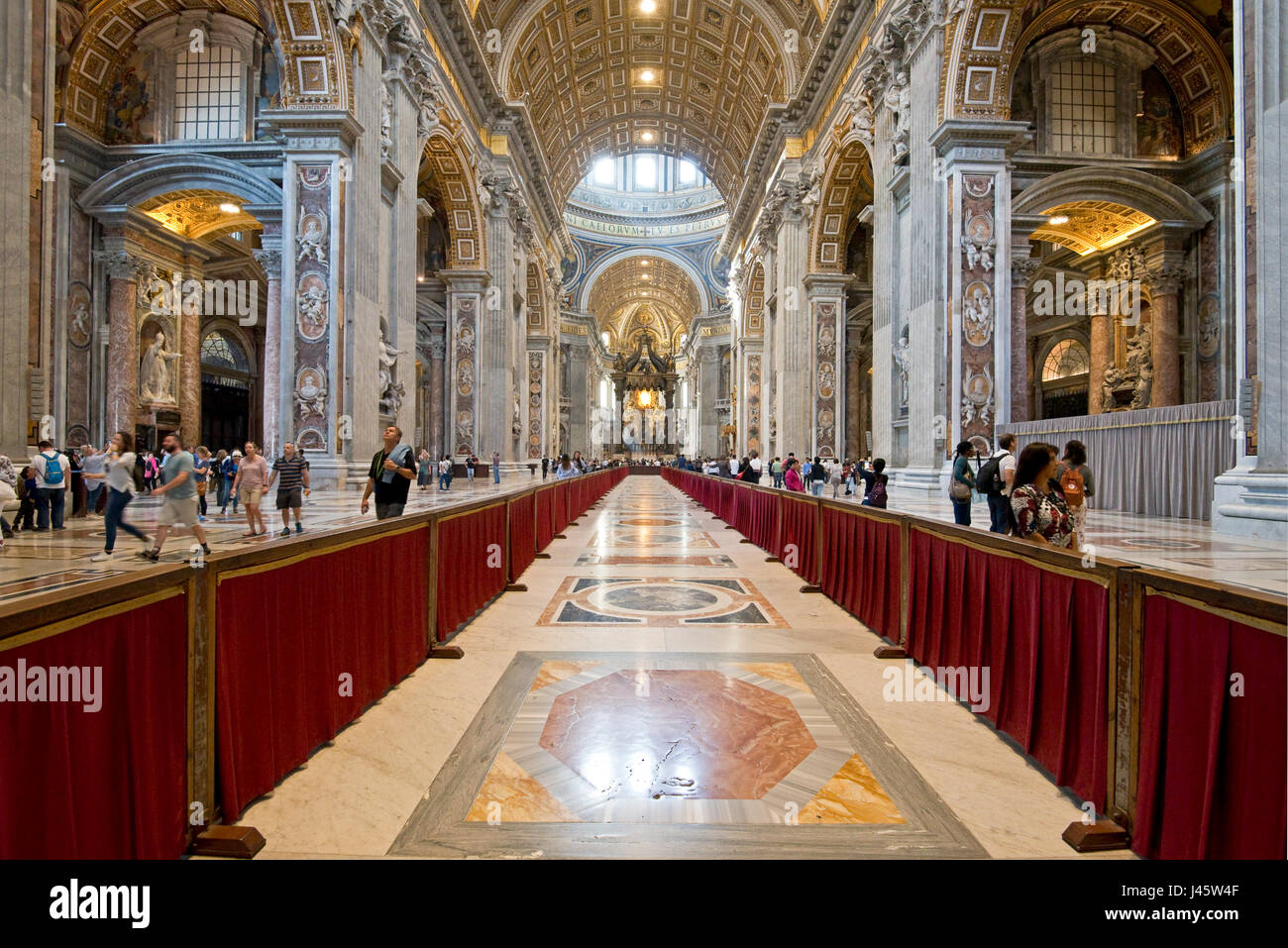 A wide angle interior view inside St Peter's Basilica with tourists walking around. Stock Photo