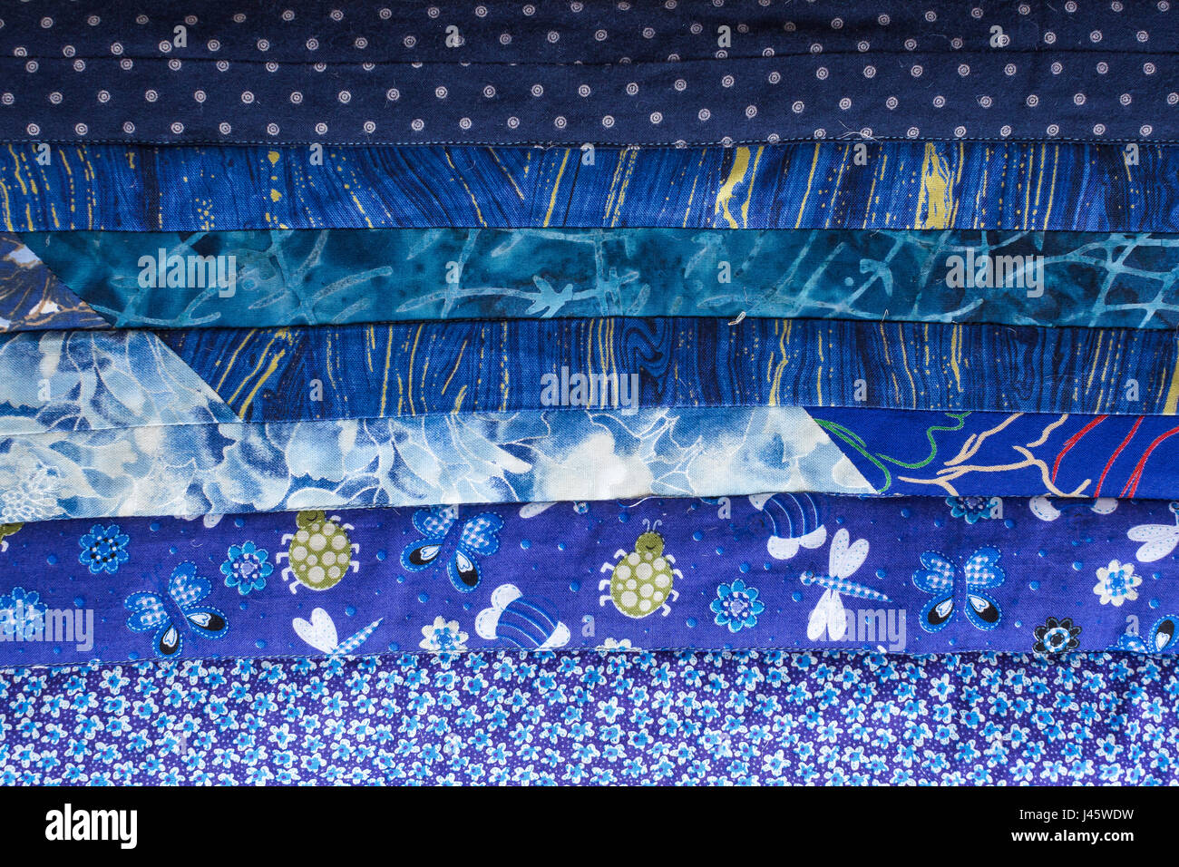 handcraft, patchwork, stitching, home atmosphere concept - textile background here is a beautiful coverlet in intense blue shades with horizontal strips sewed of patches with various abstract prints Stock Photo